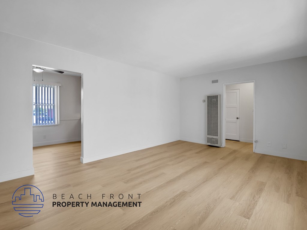 A room with wooden flooring and white walls, with a window on the left and a door on the right.