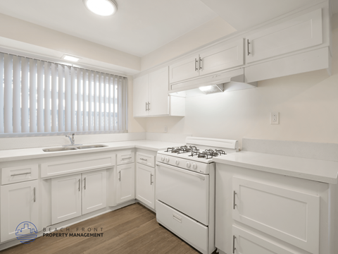 A white kitchen with a stove top oven and cabinets.