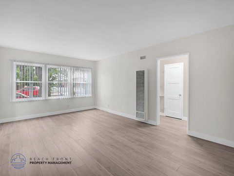 A spacious room with wooden flooring and a window with blinds.