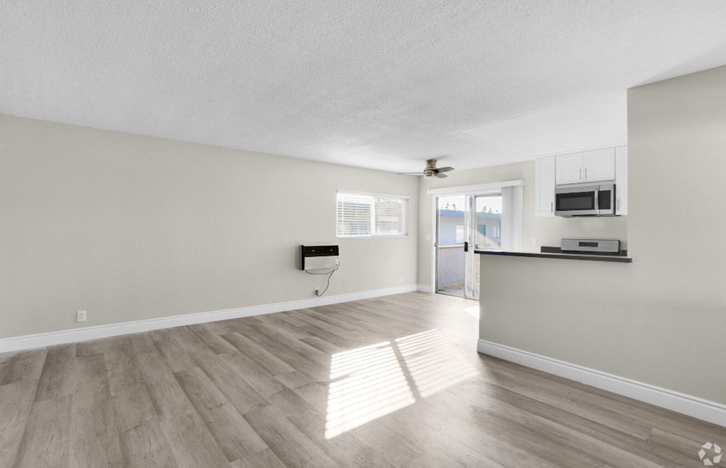 the living room and kitchen of an apartment with white walls and wood floors