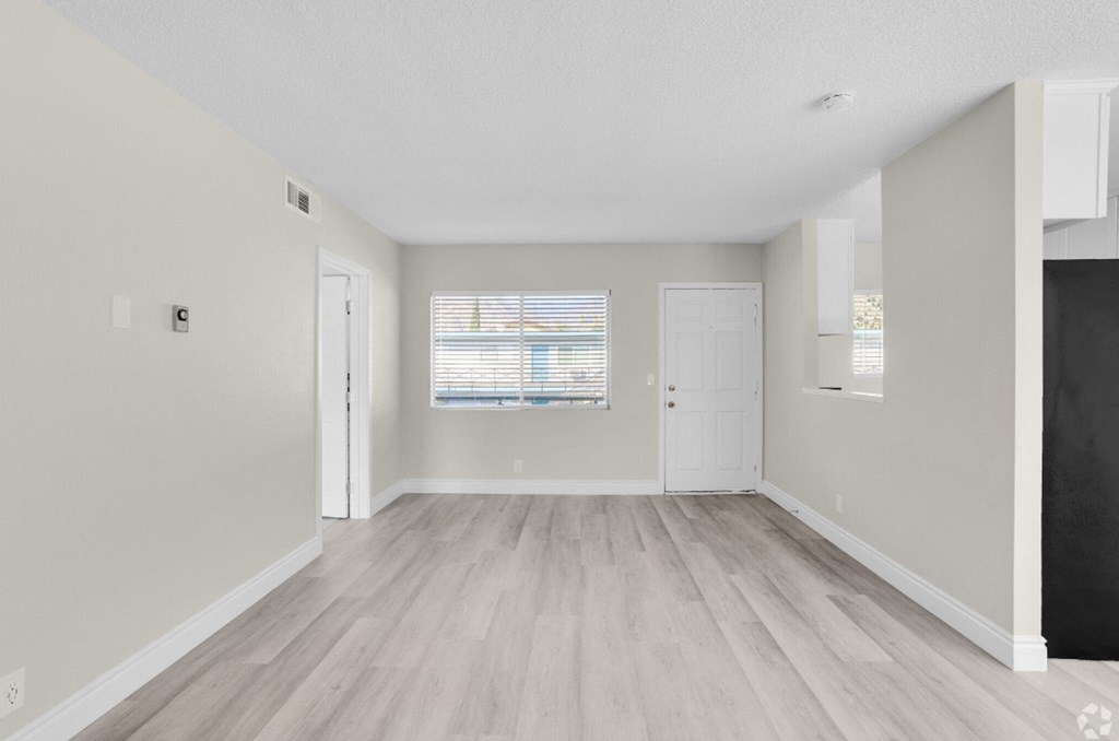 the living room and dining room of an apartment with white walls and wood floors