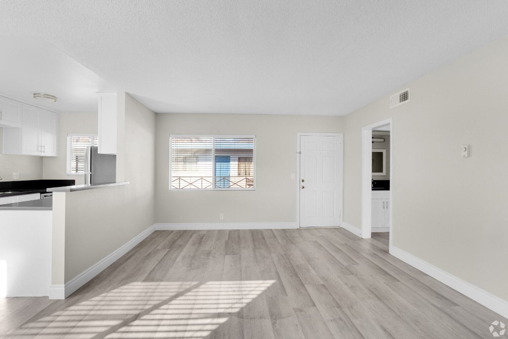 the living room and kitchen of an apartment with white walls and wood flooring