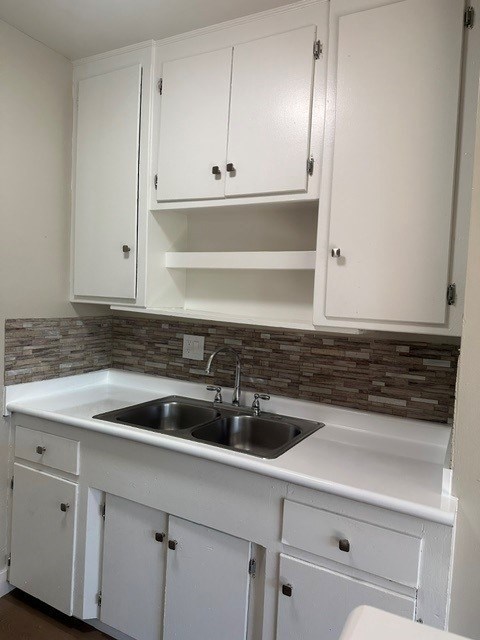 A kitchen with white cabinets and a stone backsplash.