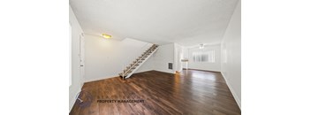 A spacious room with wooden floors and a staircase.