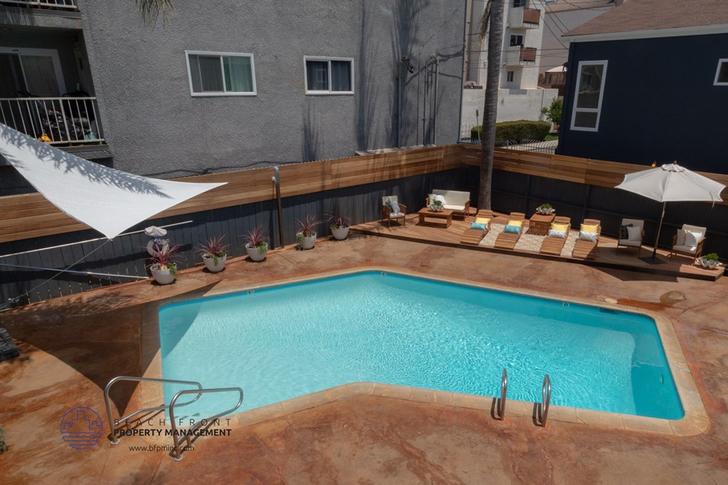 A small pool with a white umbrella and a table with chairs around it.