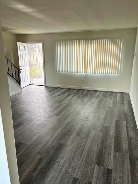 an empty living room with wood flooring and a door to a balcony