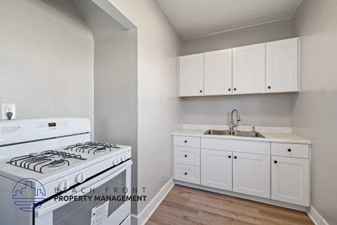 A kitchen with a stove, sink, and cabinets.
