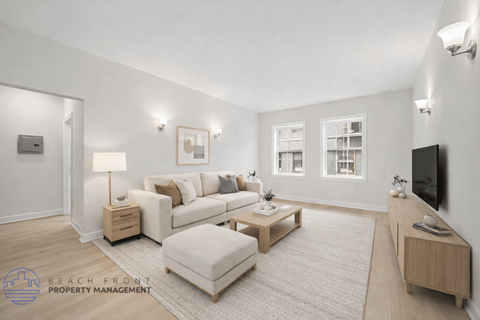 A well-lit living room with a white couch, a white ottoman, and a wooden coffee table.