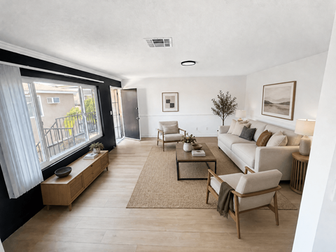 A living room with a white couch, wooden coffee table, and a large window with white curtains.