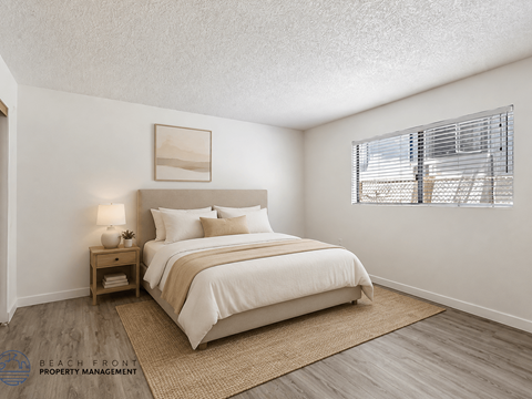 A bedroom with a large bed, a nightstand with a lamp, and a window with blinds.