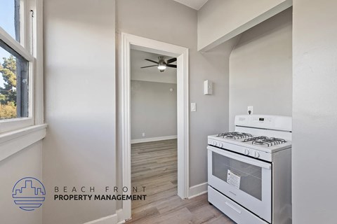 A modern kitchen with a stove top oven and a fan in the doorway.