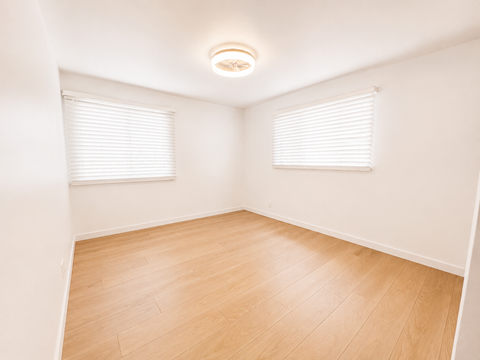A room with wooden flooring and two windows with blinds.