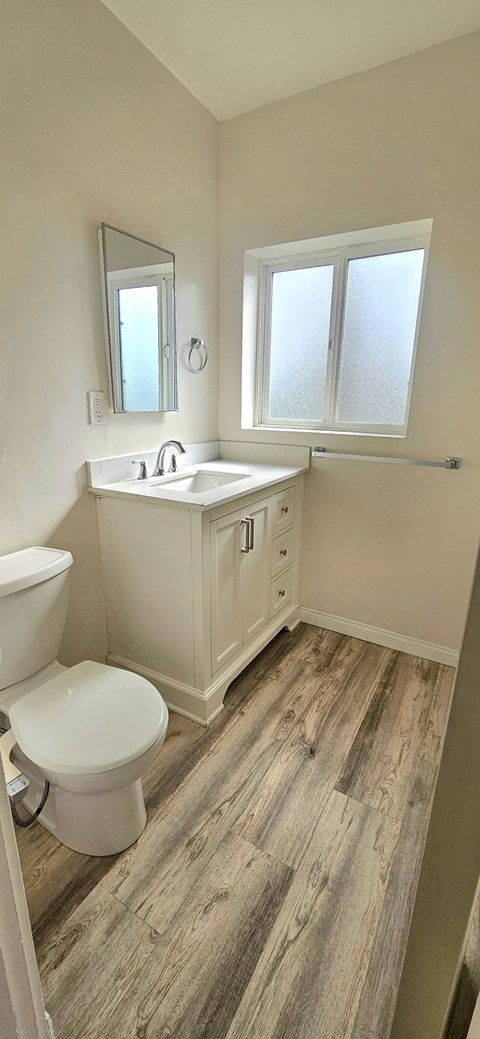 A bathroom with a white sink, toilet, and wooden flooring.