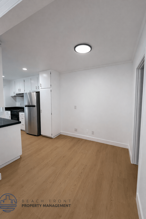 A kitchen with white cabinets and a black countertop with a stainless steel refrigerator.