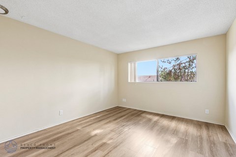 A room with wooden flooring and a window showing a tree and a building outside.