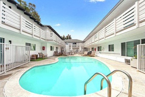 A swimming pool in a sunny day surrounded by white buildings.