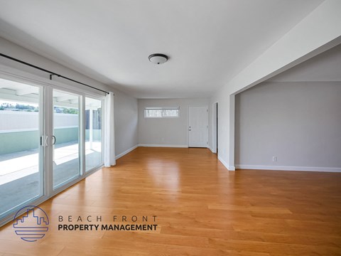 A spacious room with wooden flooring and a logo for Beach Front Property Management in the corner.