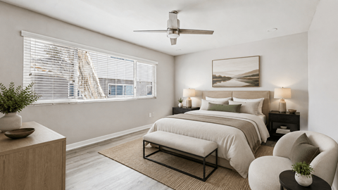 A bedroom with a large bed, a ceiling fan, and a window with blinds.