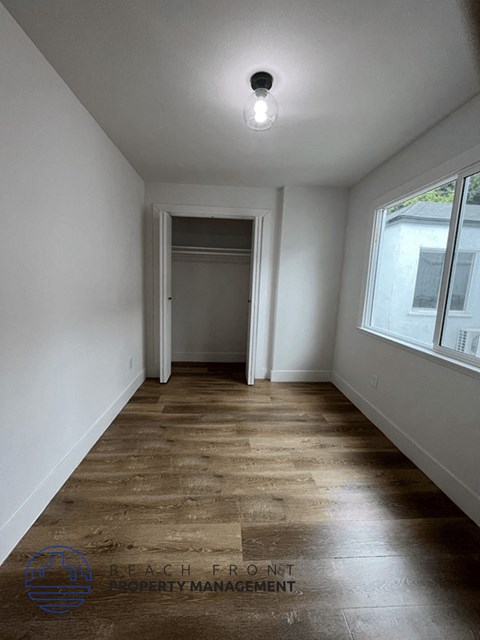 a room with white walls and wood floors and a door to a closet