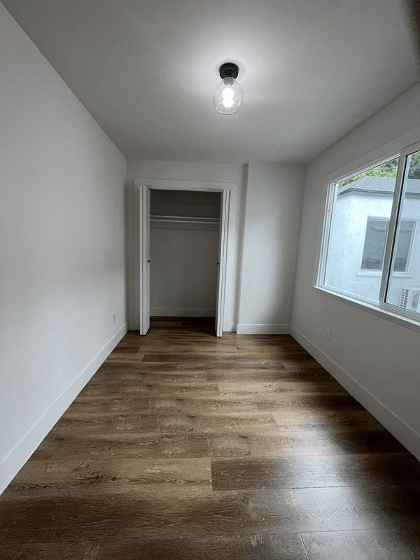 a bedroom with a large window and hardwood floors