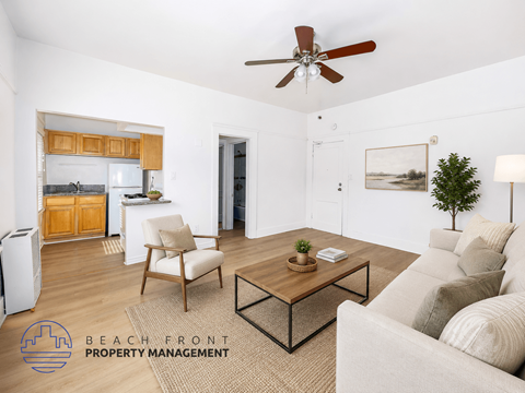 A living room with a couch, chair, and coffee table with a logo for Beach Front Property Management.