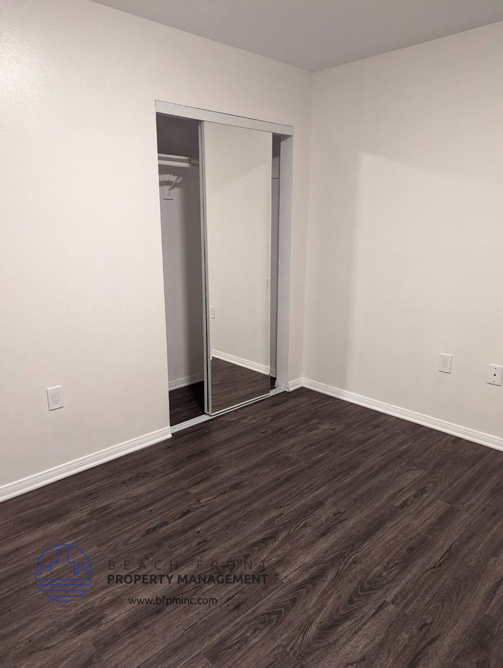 a bedroom with white walls and wood flooring and a closet