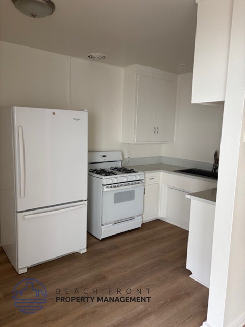 A white refrigerator and stove in a kitchen with wooden floors and white cabinets.