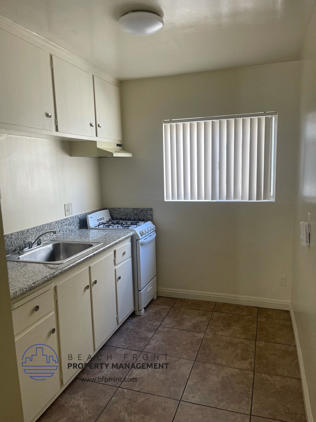 an empty kitchen with white cabinets and a sink and a window