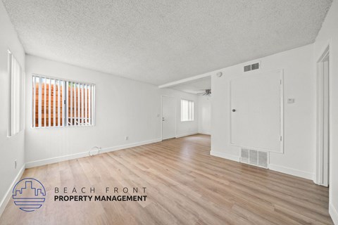 A spacious room with wooden flooring and white walls, with a window covered by orange blinds.