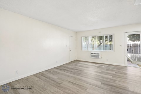 A spacious room with wooden flooring and a window with blinds.