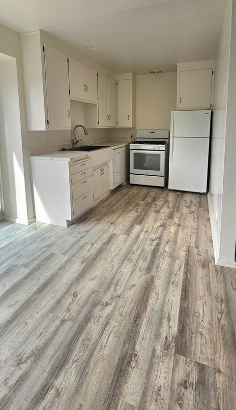 A kitchen with white appliances and wooden floors.