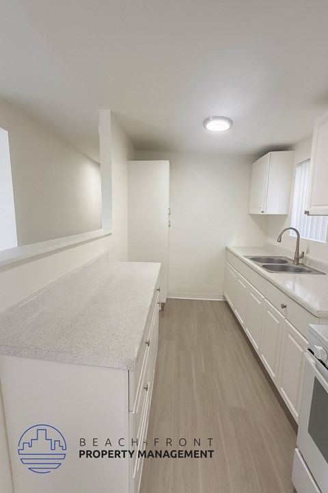 A kitchen with white cabinets and a logo for Beachfront Property Management.