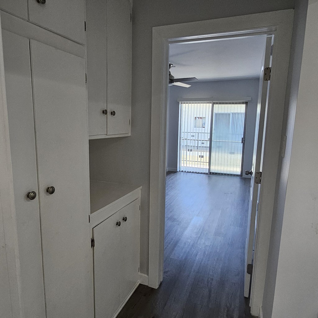 a small kitchen with white cabinets and a hallway to a living room
