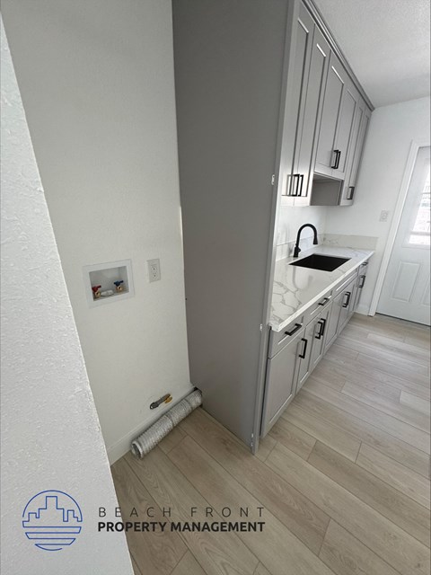 A kitchen with a white counter top and wooden flooring.