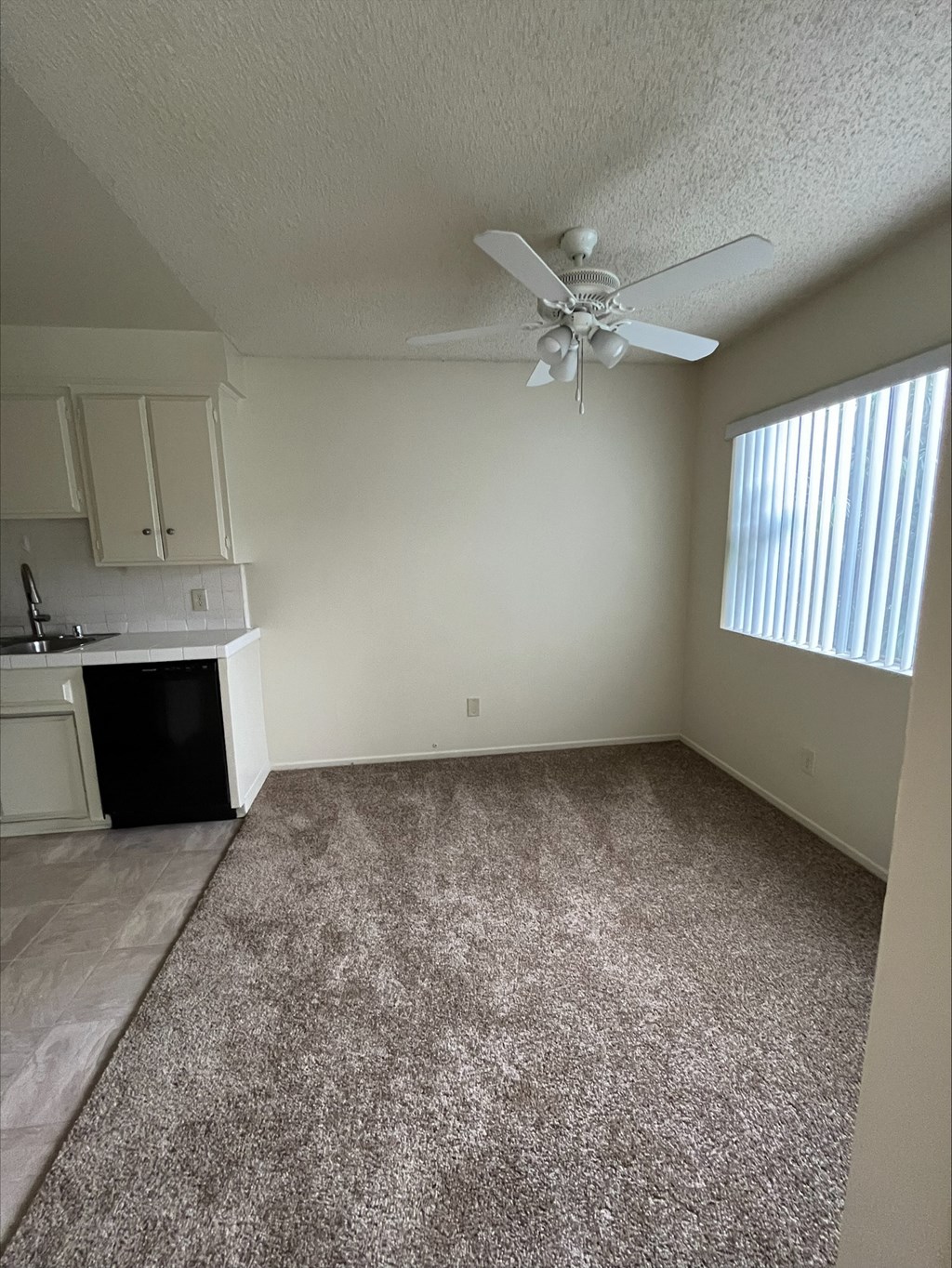an empty living room with a ceiling fan and a kitchen