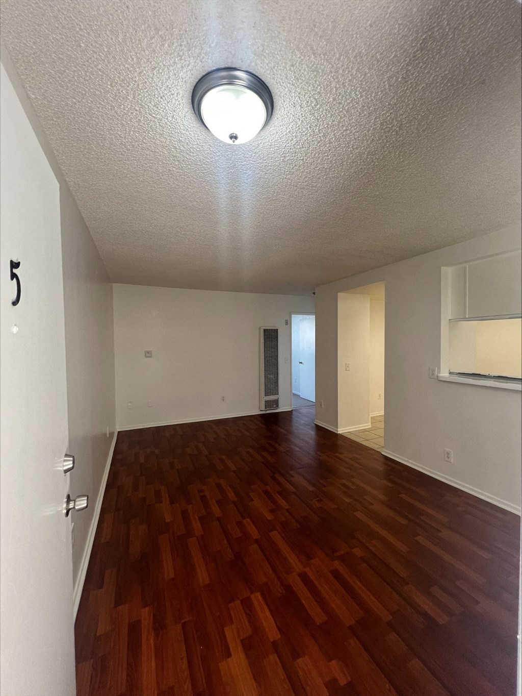an empty living room with wood flooring and a ceiling light