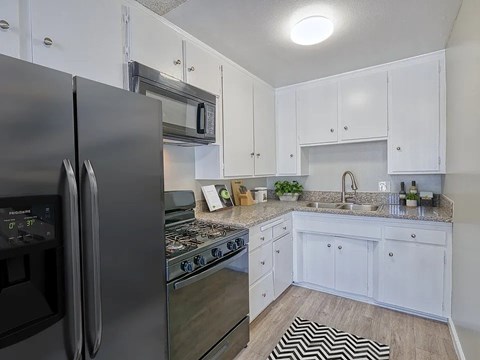 A black refrigerator is in a kitchen with white cabinets.