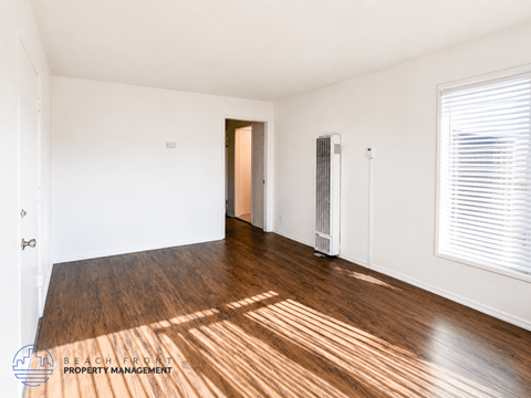 A room with wooden floors and white walls, with a door and a window.