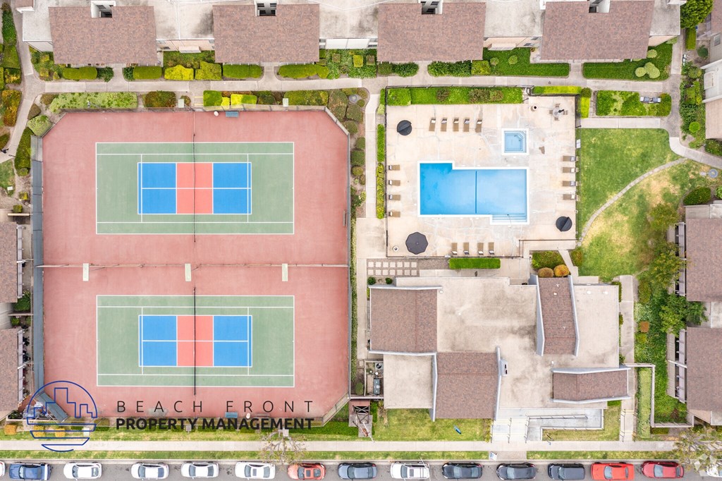 An aerial view of a tennis court and a pool surrounded by houses.
