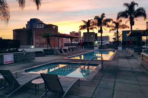 a pool with chairs and a city at sunset