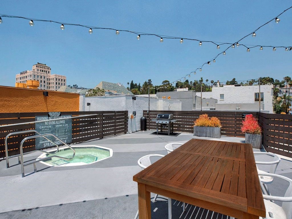 the deck of a roof top patio with a pool and a table