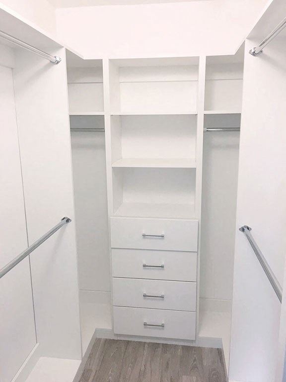 a walk in closet with white shelves and drawers