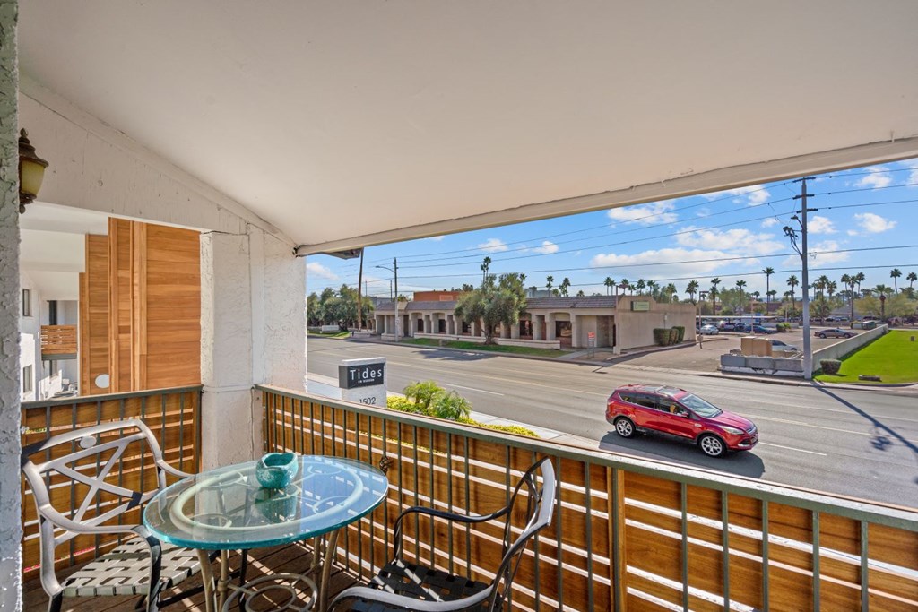 a balcony with a glass table and chairs and a red car parked on the street