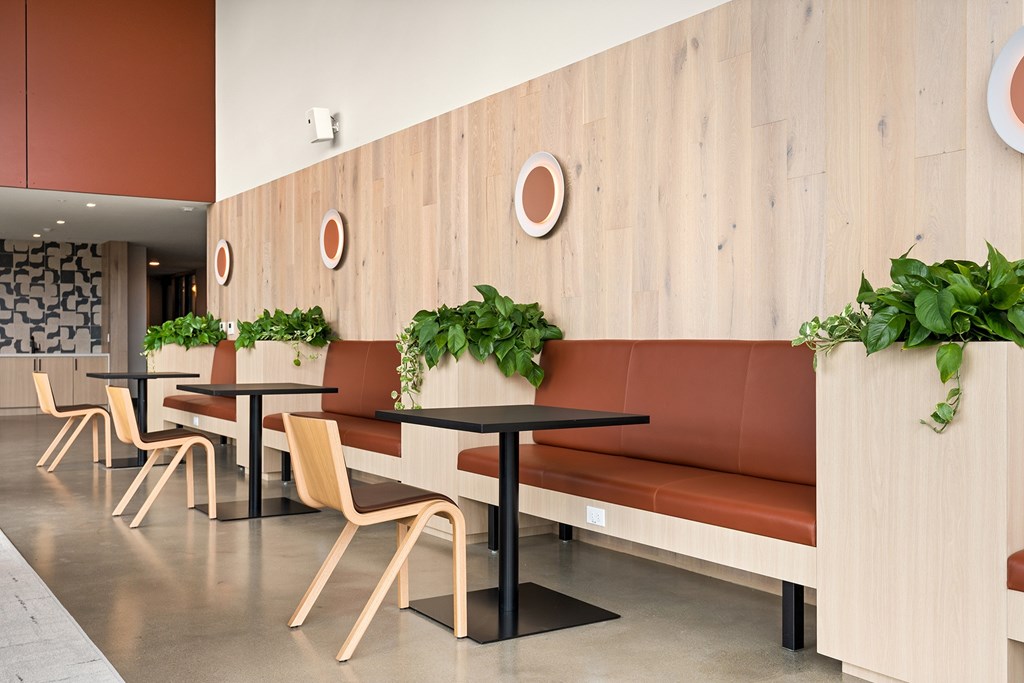 A long wooden bench with a black base is in the middle of a room with tables and chairs.