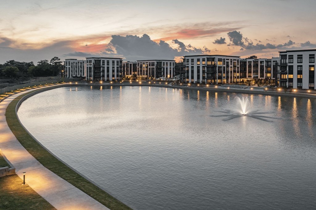 a fountain in the middle of a lake with buildings in the background