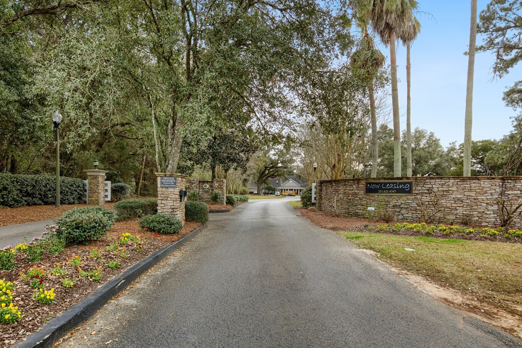 a driveway with a stone wall and trees on the side of a road