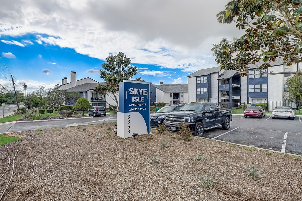 a sign in front of an apartment complex with cars parked in the parking lot