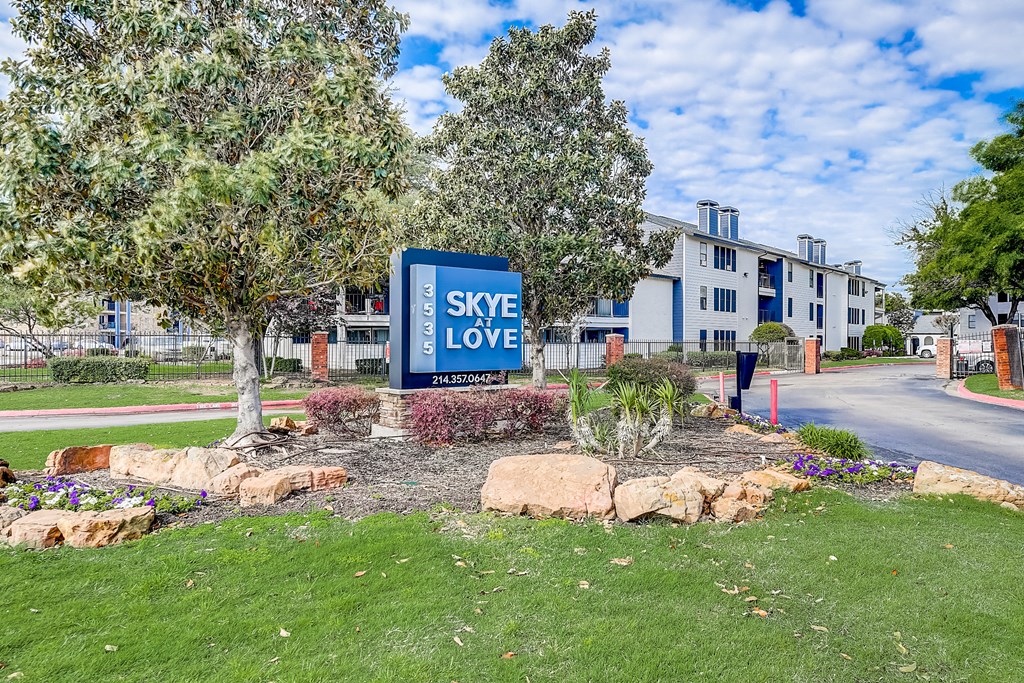 a blue sign that says sky love in the middle of a grassy area with trees and