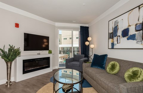 A living room with a grey couch, a glass table, a fireplace, and a painting on the wall.