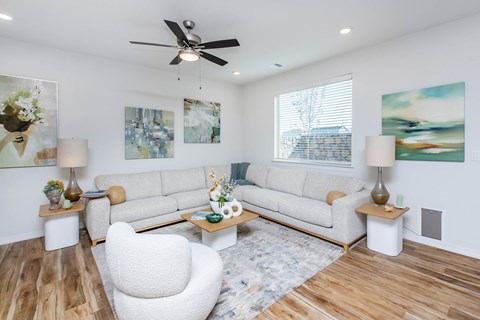 A living room with a white chair, a white couch, and a ceiling fan.